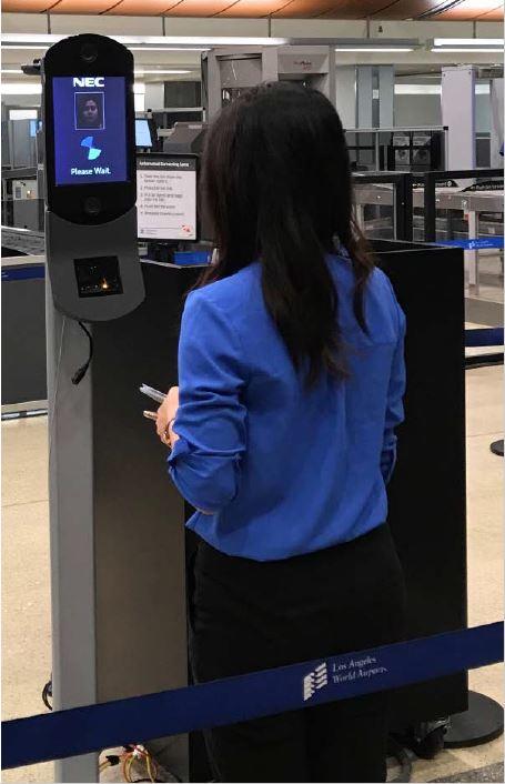A woman stands facing a small screen that's about five feet off the ground on a pedestal. This is an example of a face recognition kiosk from TSA's website.